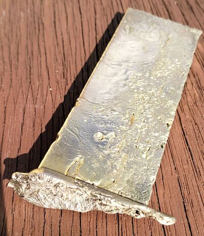 A first brass ingot after cooling, showing the surface texture and excess metal at the end of the pour